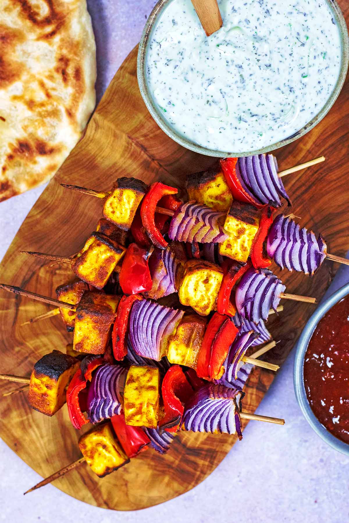 A serving board with cheese and vegetable skewers and a bowl of raita.