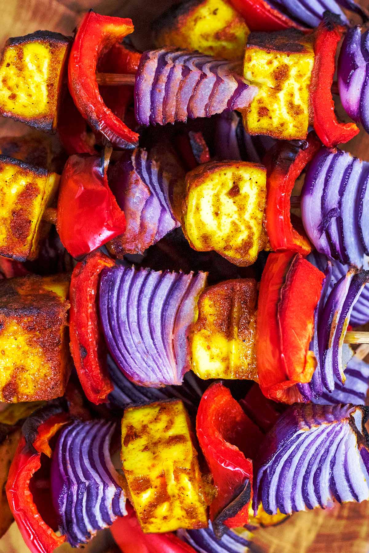 Cubes of paneer, slices of red pepper and chunks of red onion on skewers.