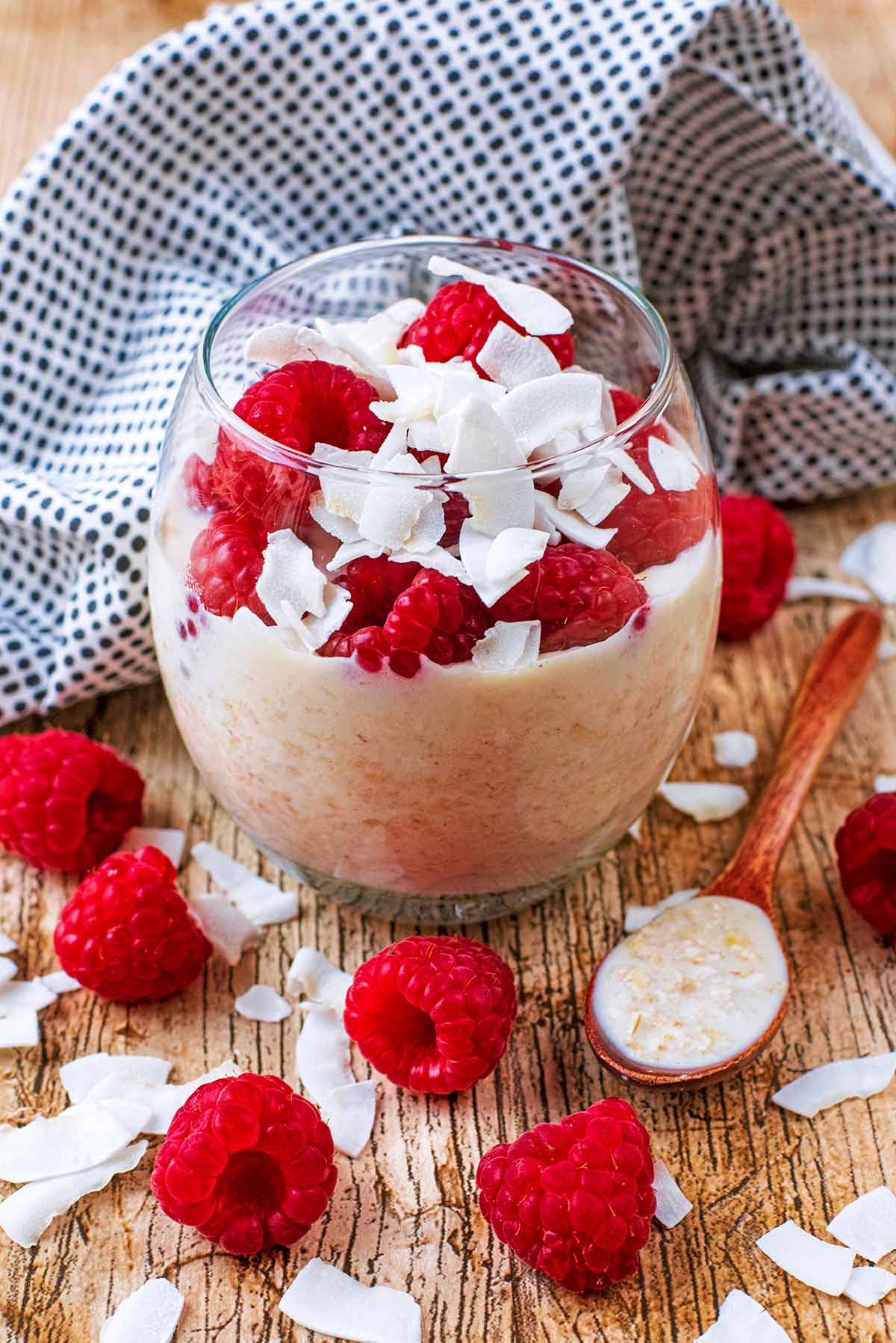 A glass of overnight oats topped with raspberries and coconut flakes.