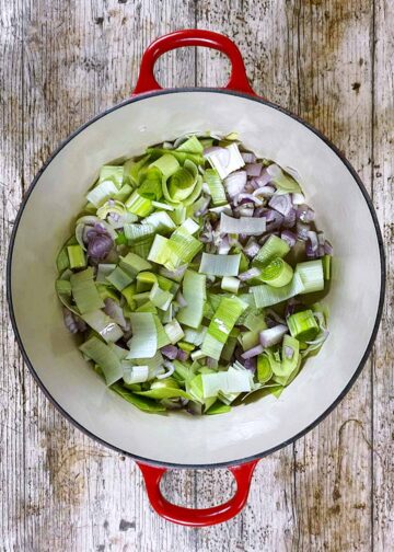 A large pan with chopped leeks and shallots cooking in it.