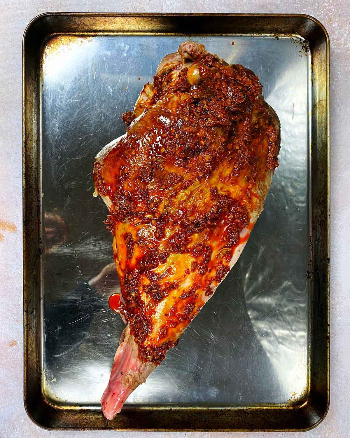 A baking tray with a whole leg of lamb covered in harissa.