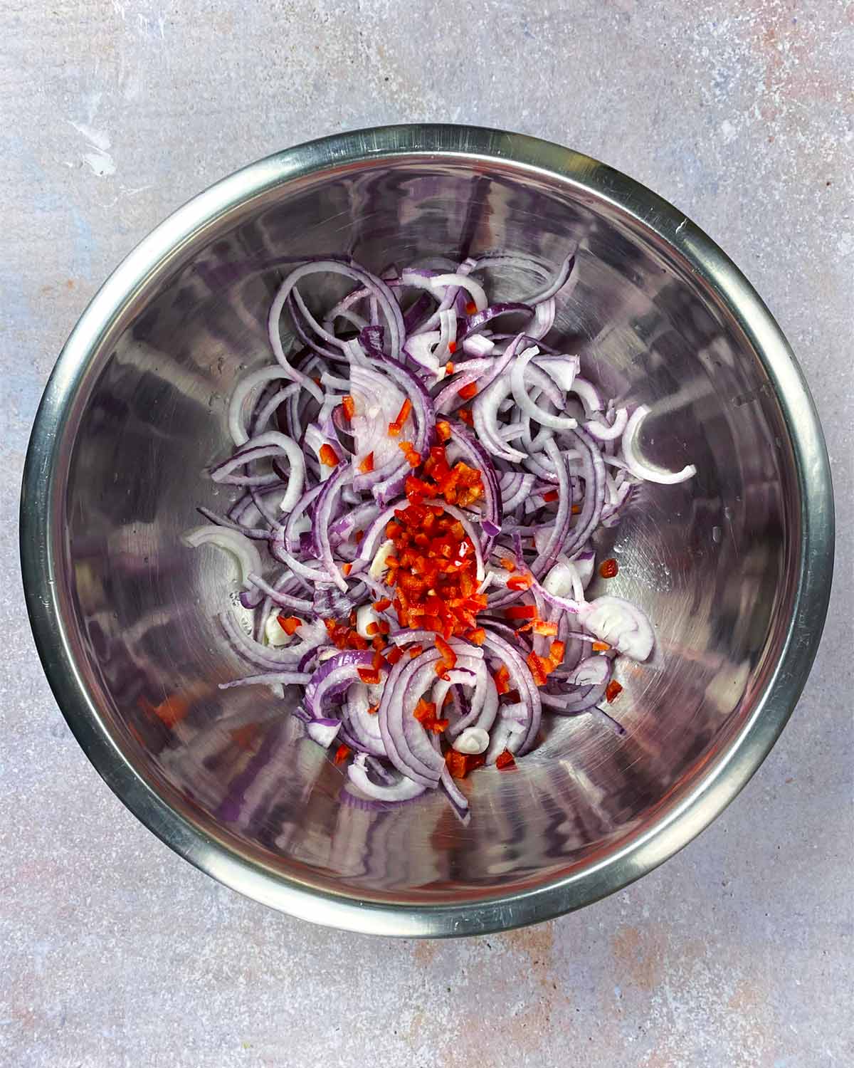 A large mixing bowl containing sliced red onion, chopped chilli and lime juice.