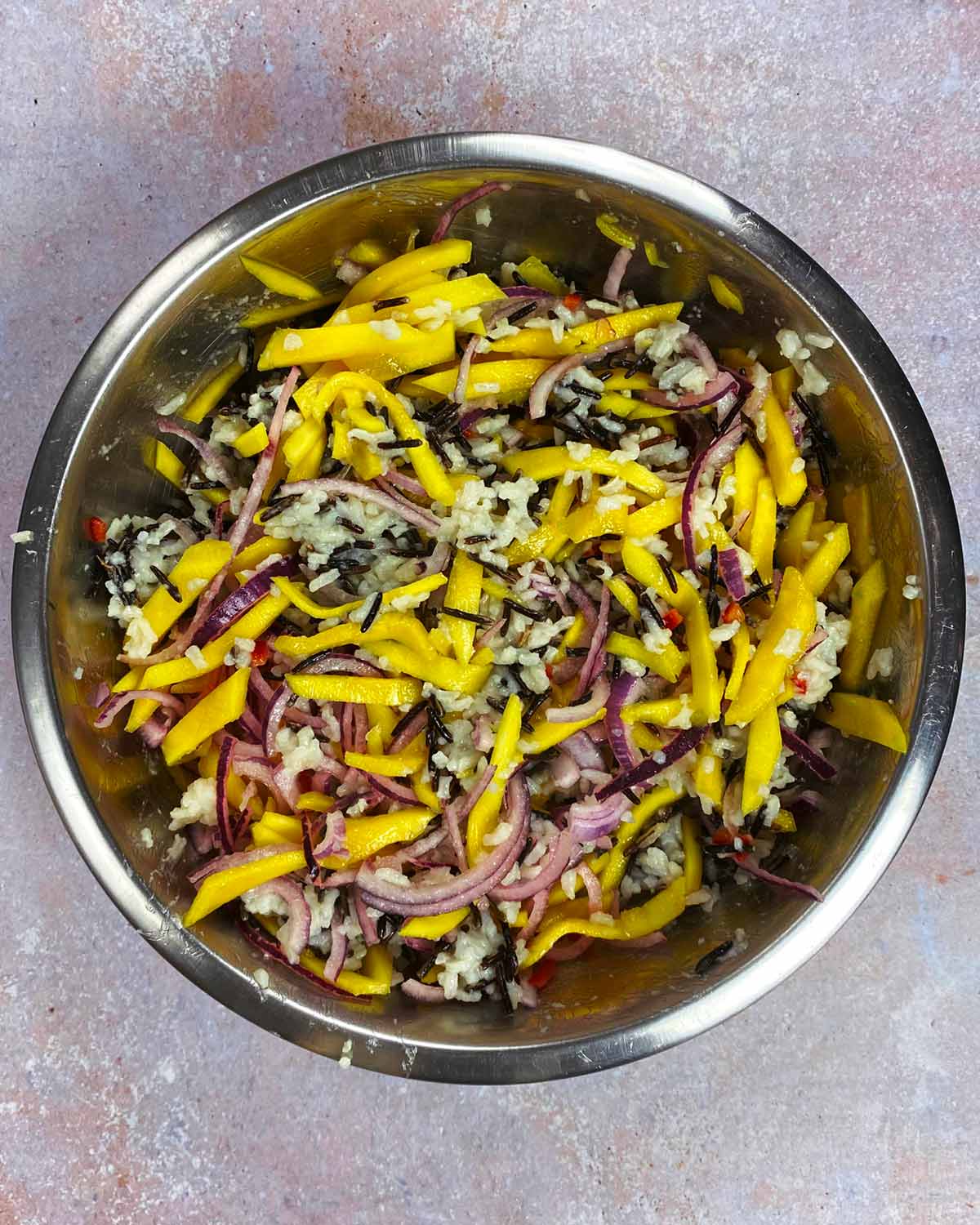 A bowl containing cooked rice, sliced onion, chopped chilli and sliced mango.