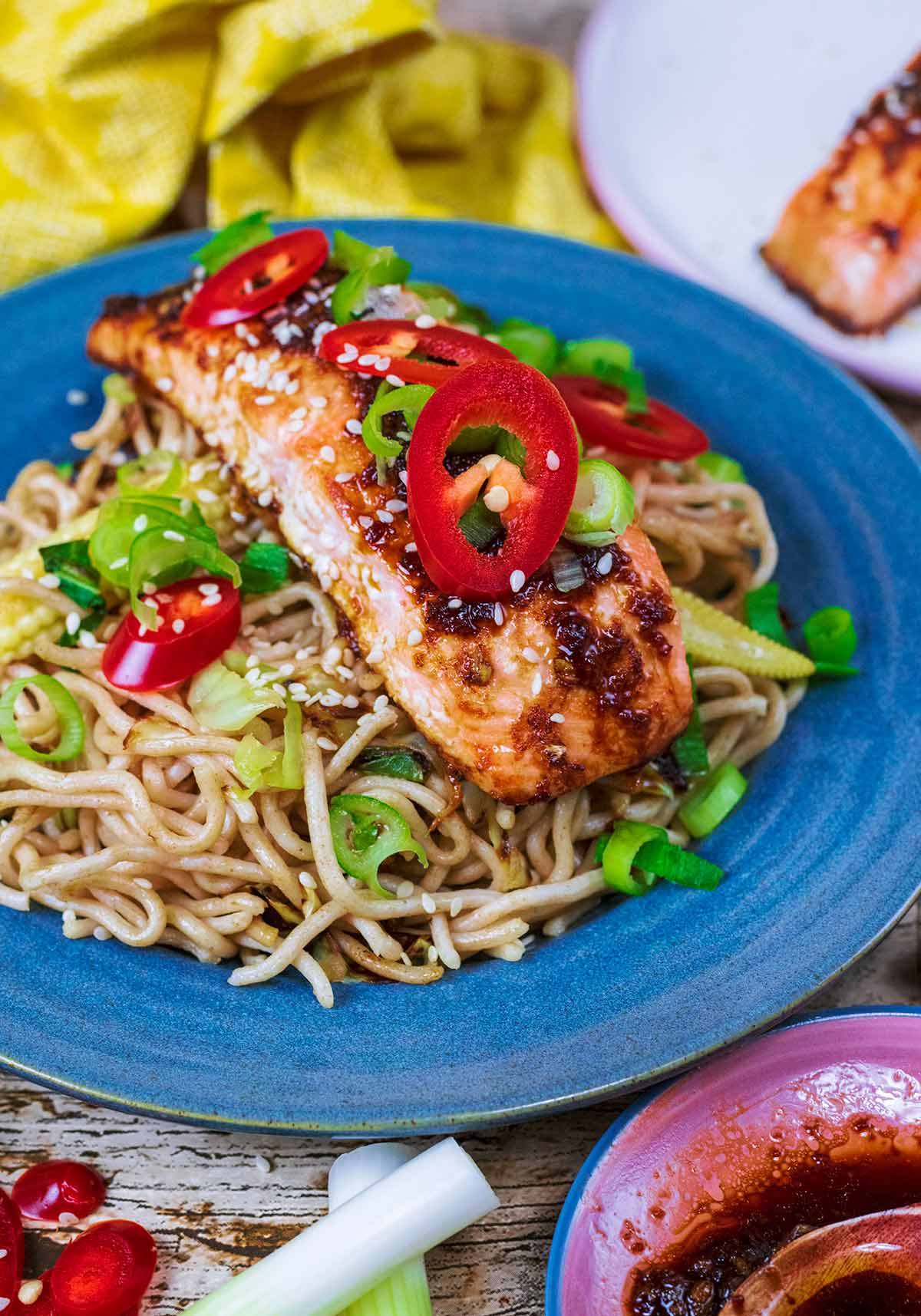 Cooked salmon on top of noodles with red chillies and spring onions.