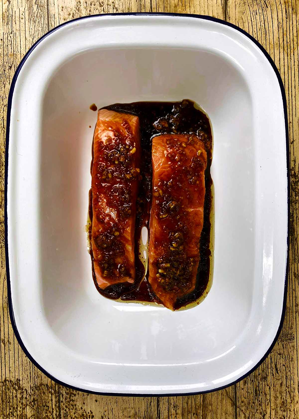 Two salmon fillets in a baking dish with marinade poured over them.