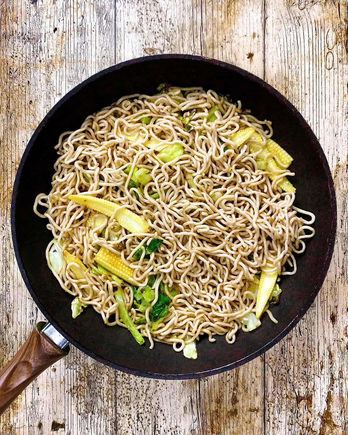 A frying pan with noodles, baby corn and cabbage stir frying.