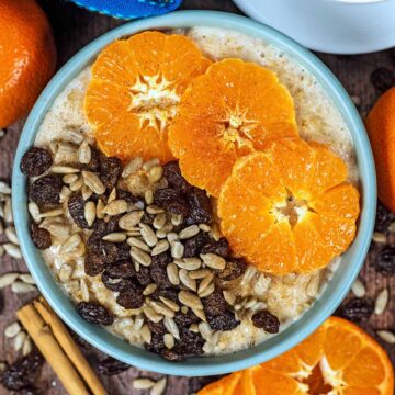 Spiced orange porridge in a blue bowl topped with sliced oranges, seeds and raisins.