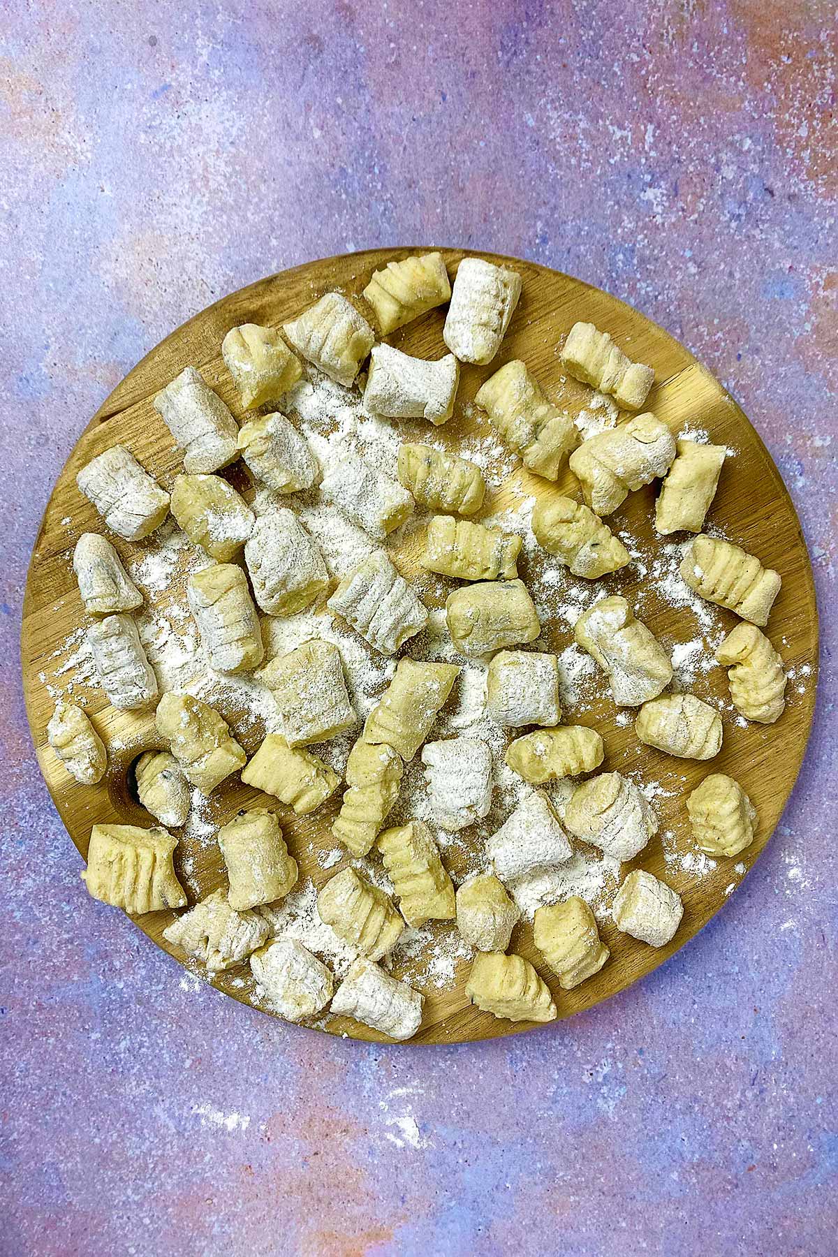 A round wooden serving board covered in uncooked gnocchi.