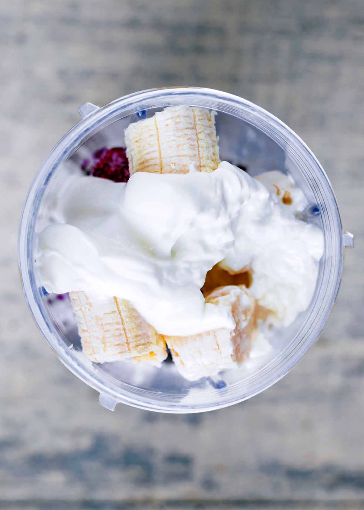 A blender jug viewed from above containing bananas, berries and yogurt.