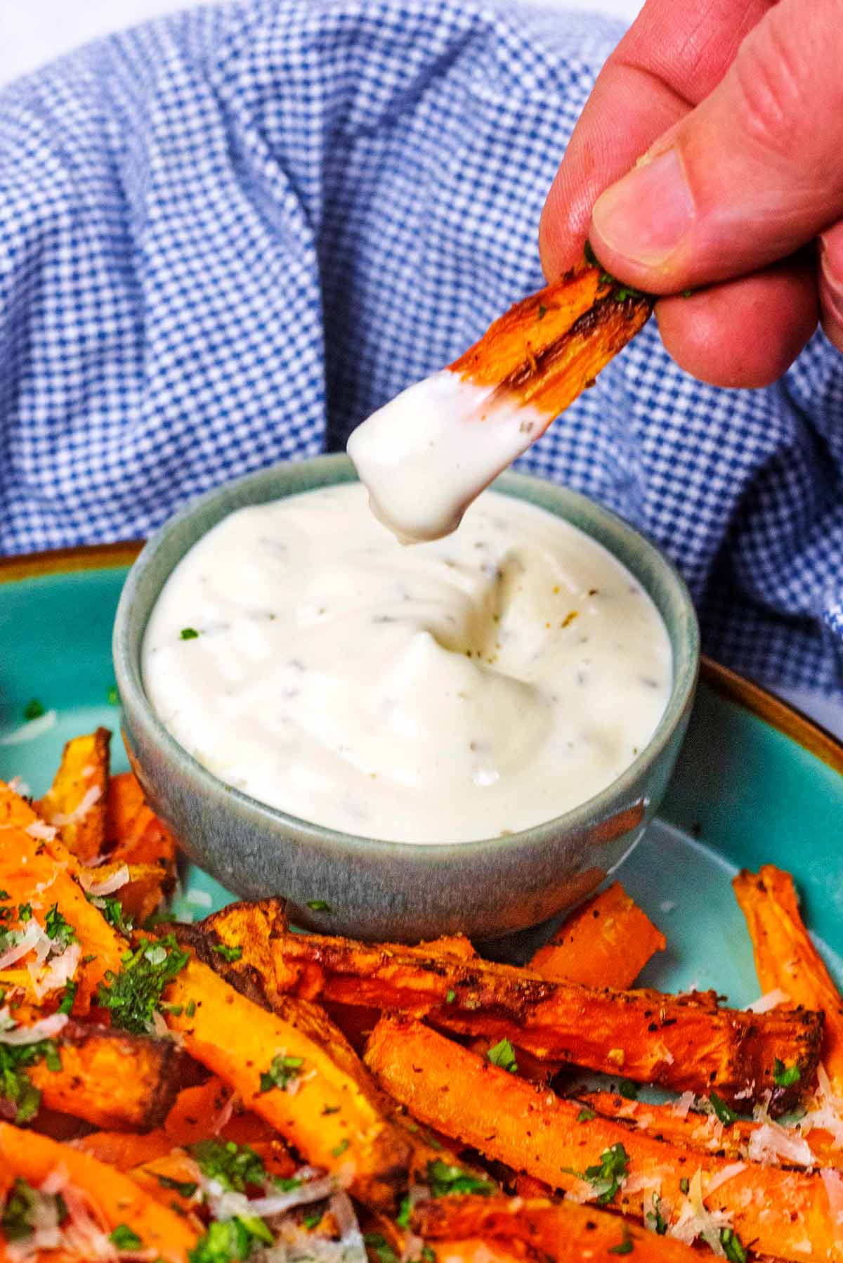 A cooked carrot being dipped into a small bowl of ranch sauce.