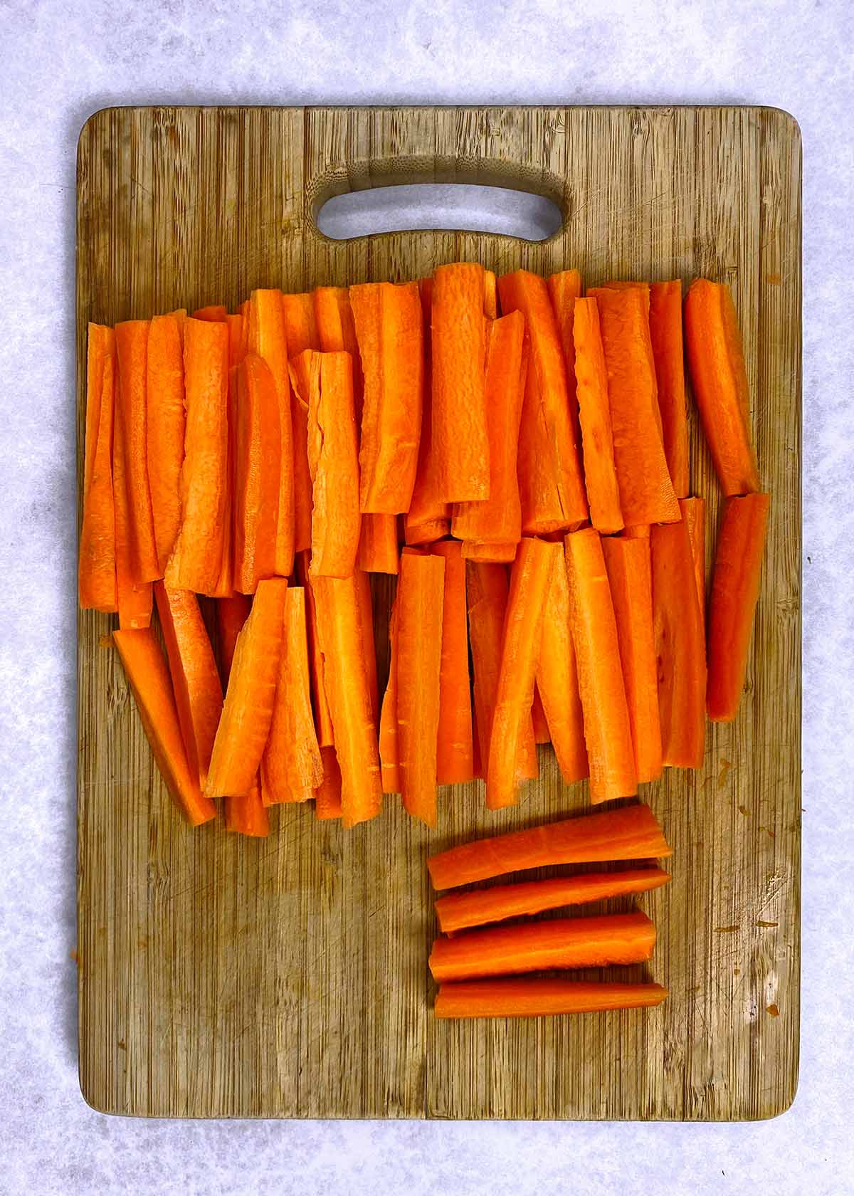 A wooden chopping board with carrots cut into battens.