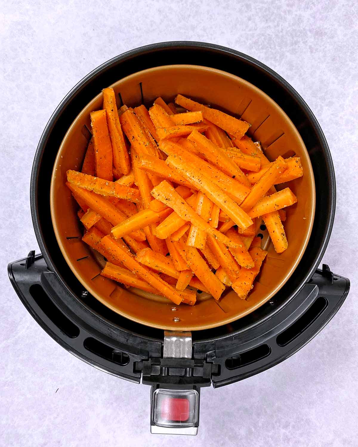 An air fryer basket containing uncooked carrot battens.