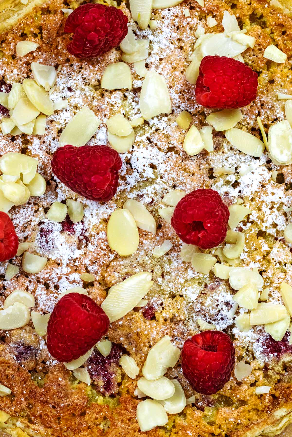 Six raspberries and some flaked almonds on a icing sugar dusted Bakewell pudding.