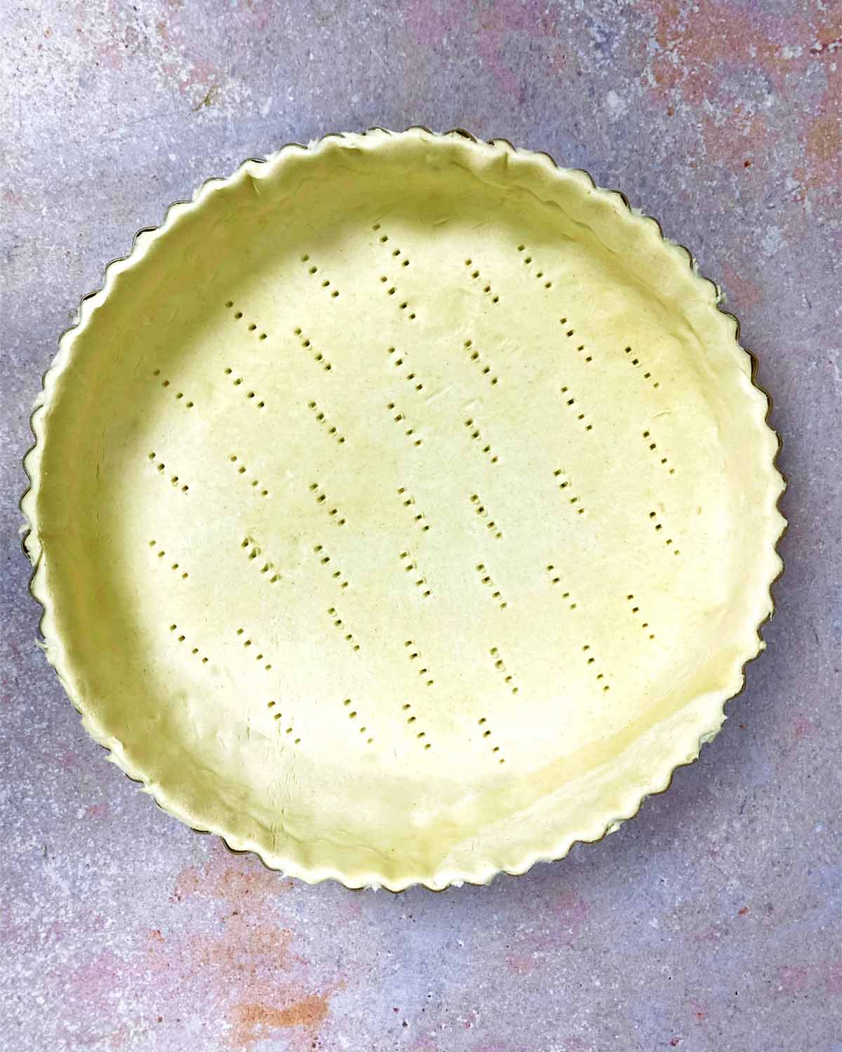 Trimmed pastry in a pie tin with the bottom pricked with holes.