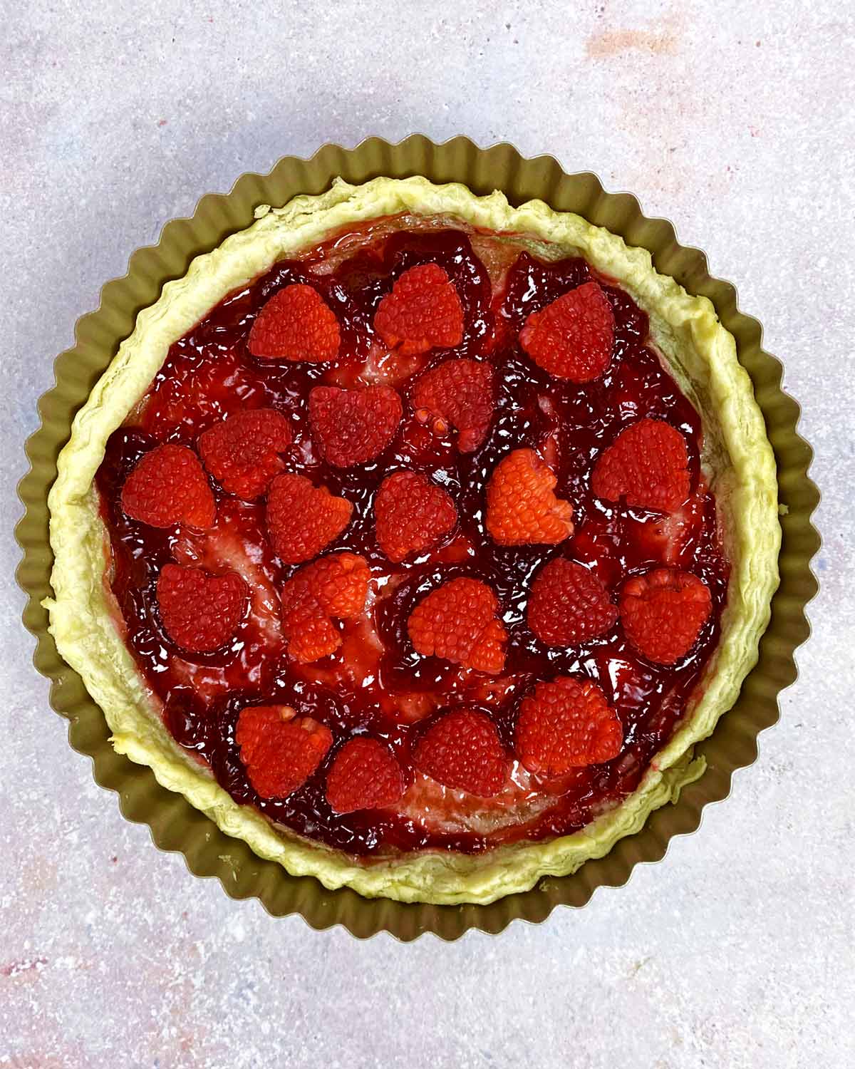 A pie crust with jam and fresh raspberries in it.