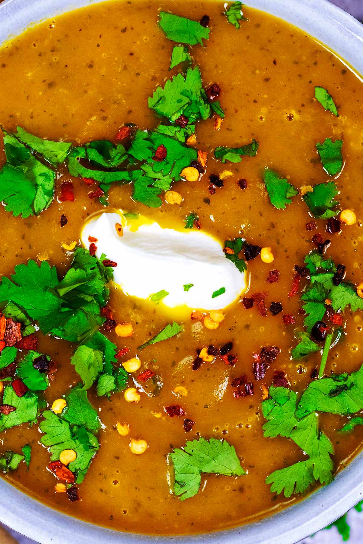 A bowl of soup topped with a dollop of cream, chopped coriander and chilli flakes.