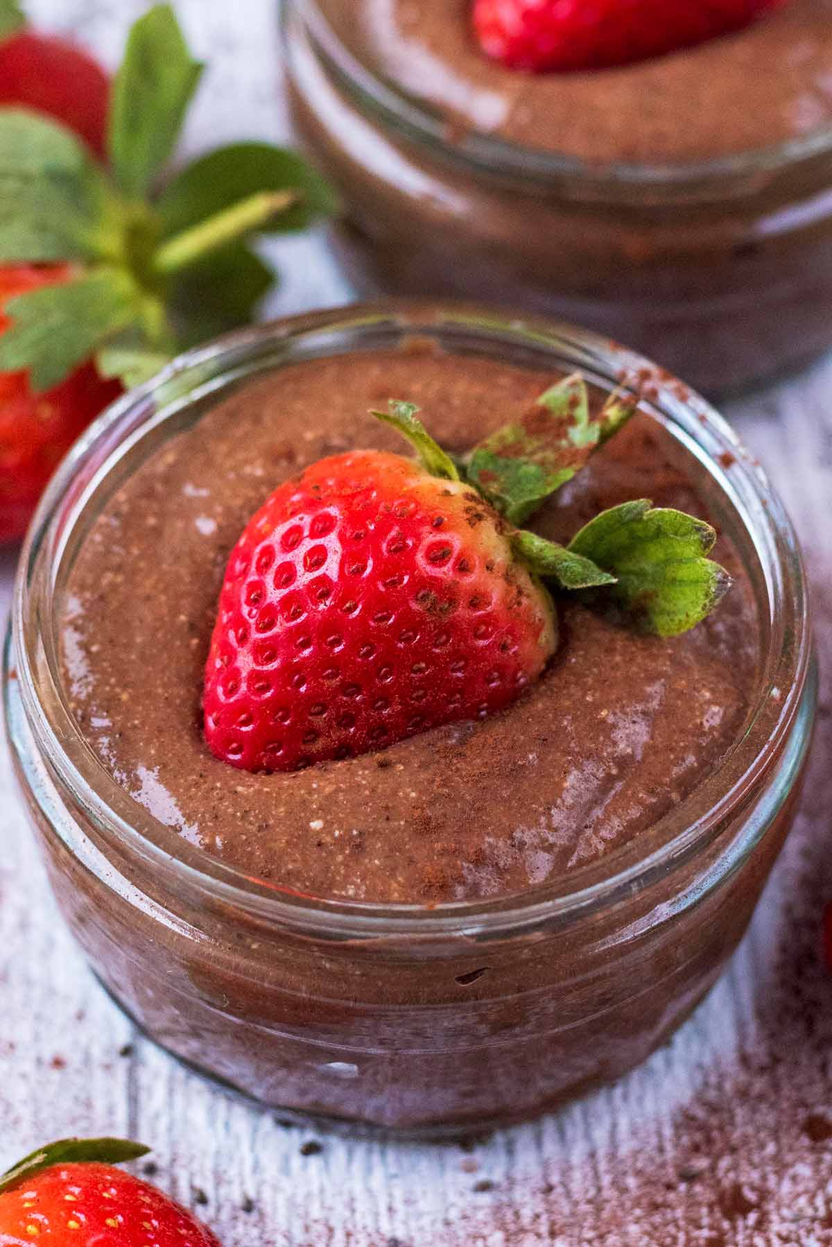 A glass ramekin containing chocolate pudding. Half a strawberry is on top.
