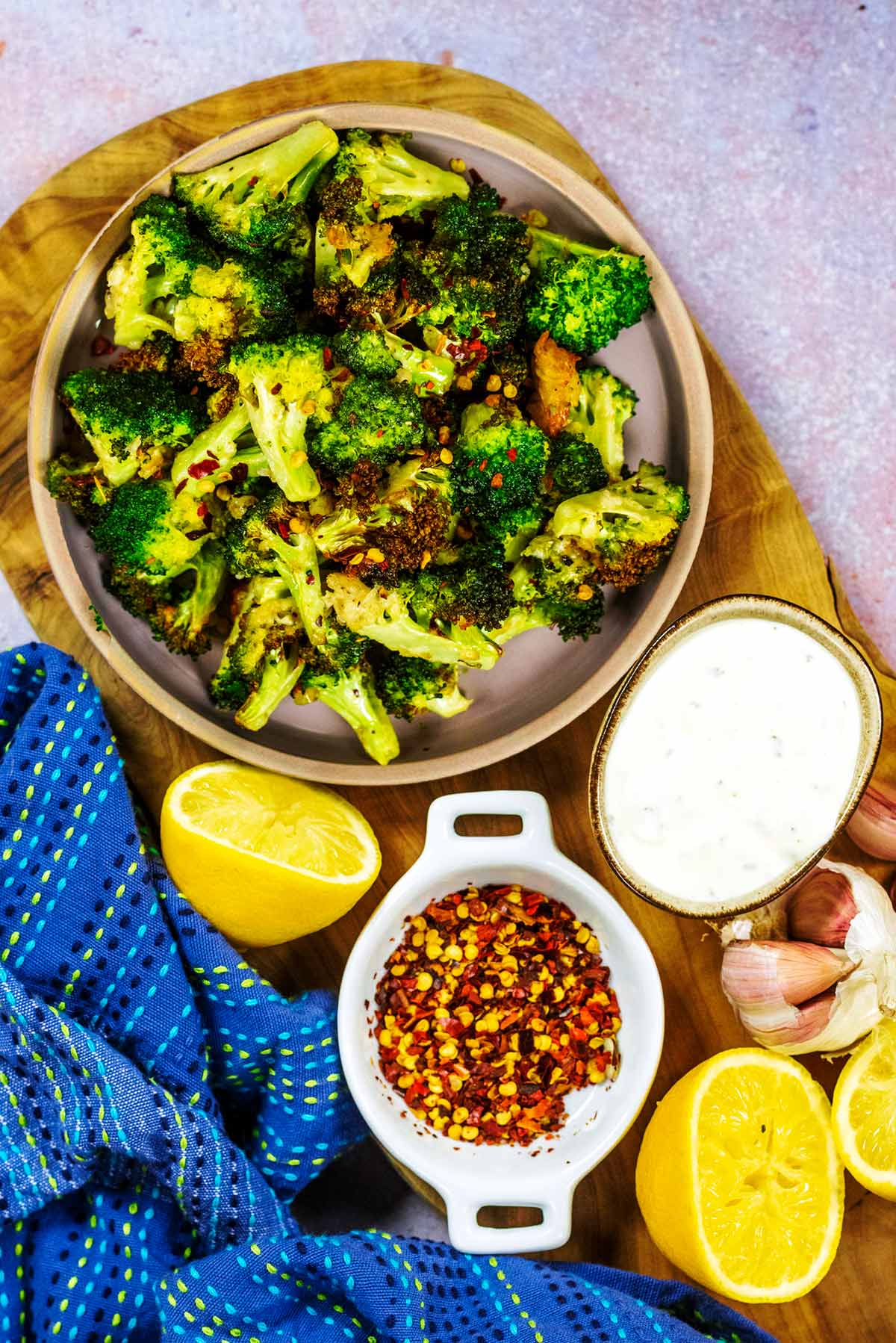 A bowl of cooked broccoli next to small bowls of dip and chilli flakes.