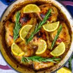 Lemon herb chicken in a round pan topped with lemon slices and rosemary sprigs.
