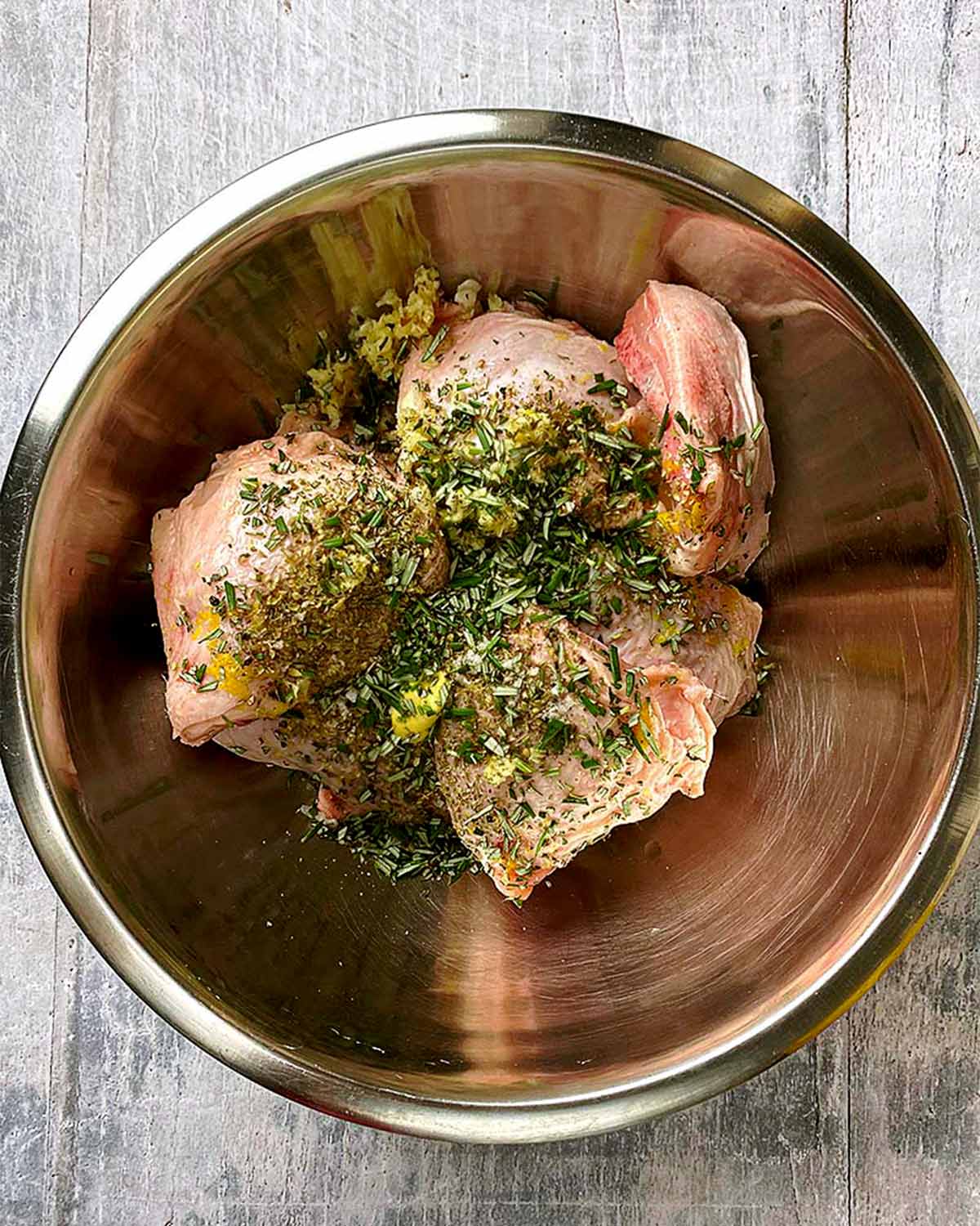A metal bowl with chicken thighs covered in chopped herbs.
