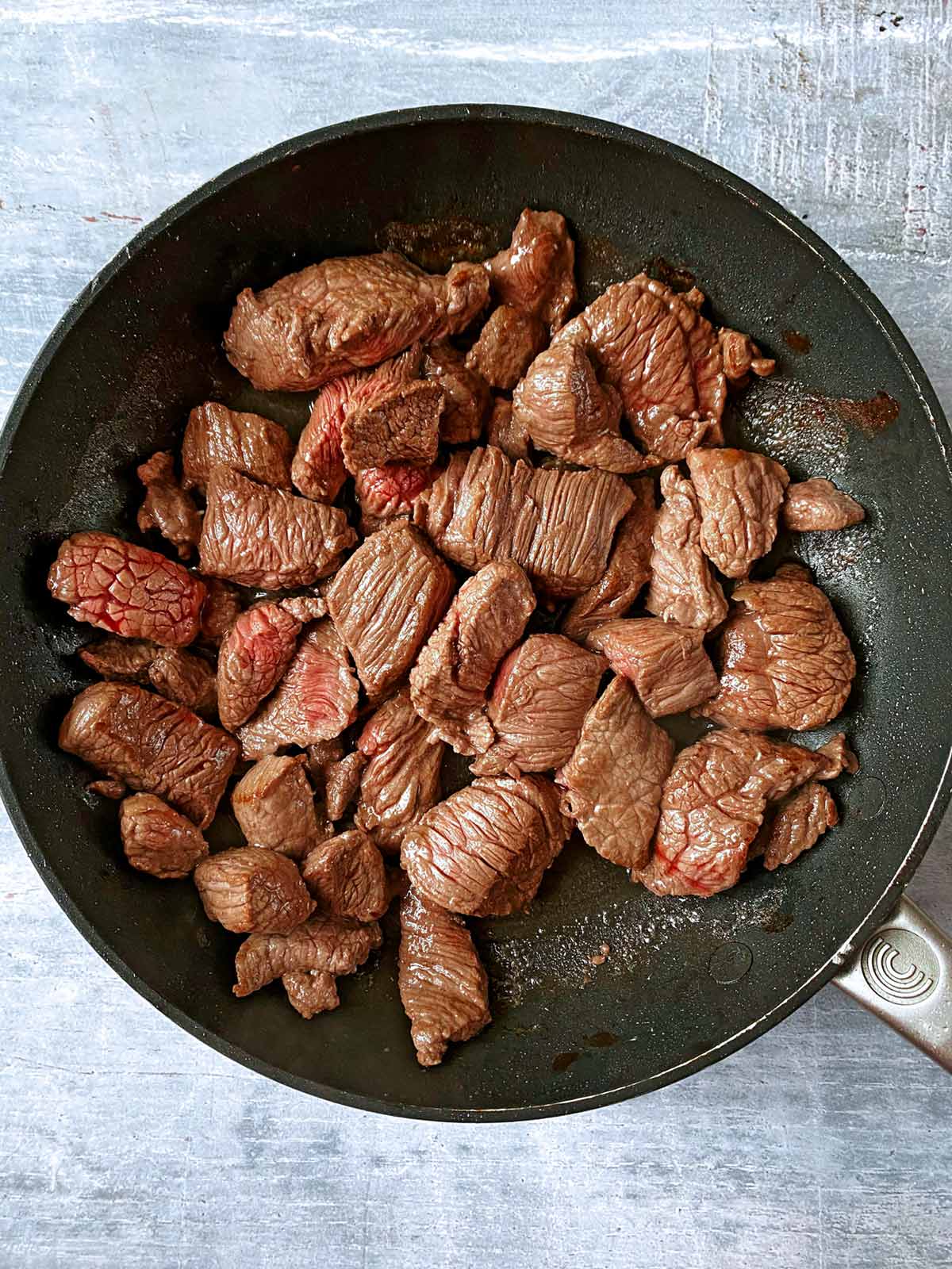 Chunks of beef cooking in a frying pan.
