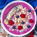 A fruit smoothie bowl topped with sliced banana, berries, nuts and oats.