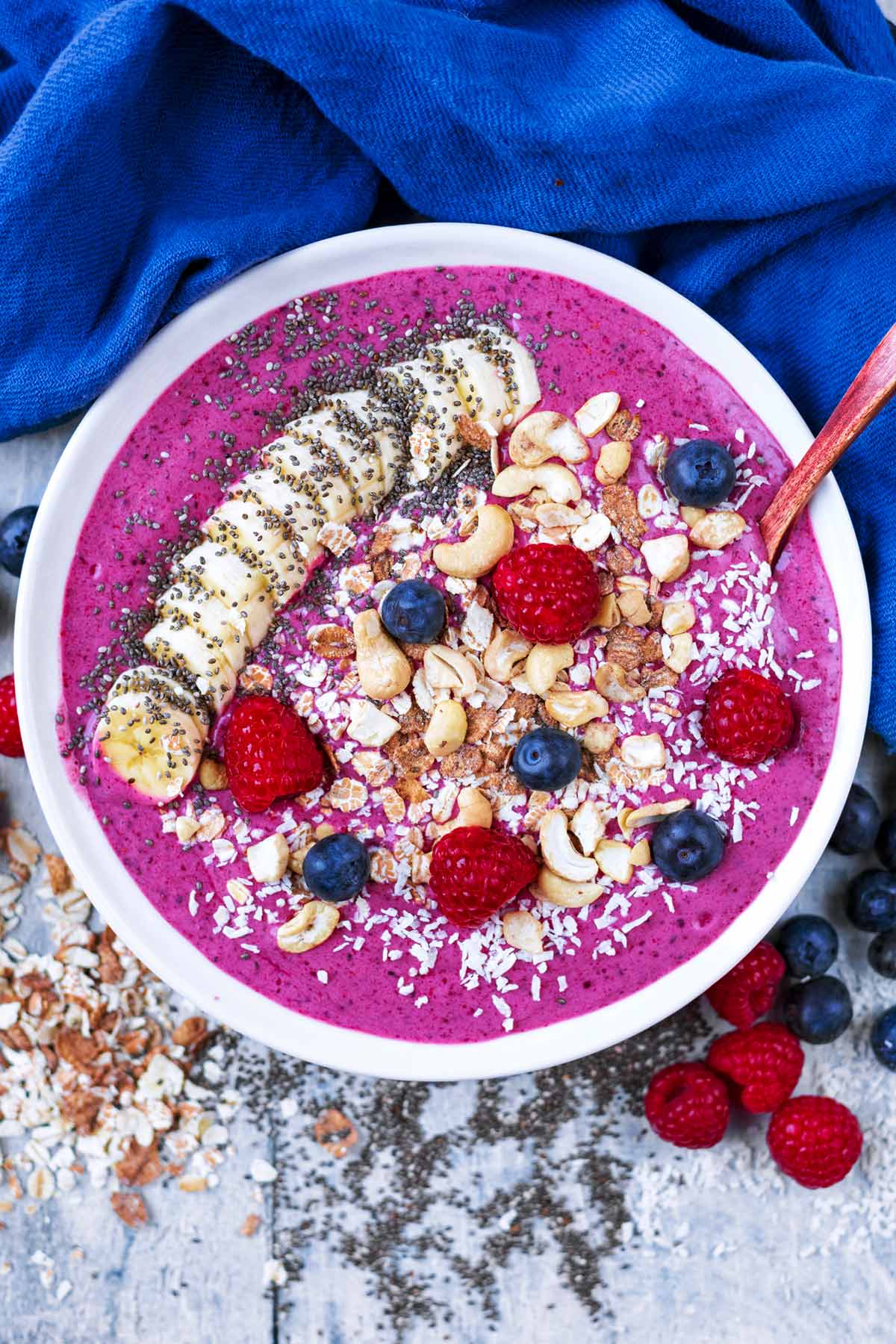 A purple smoothie in a bowl topped with fruit, nuts and seeds.