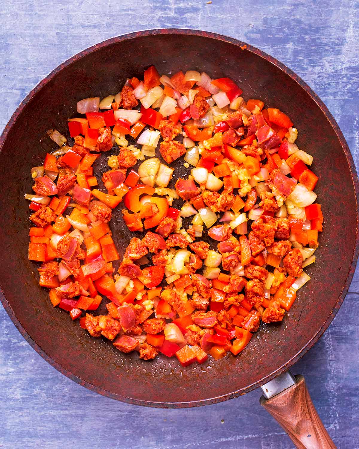 Chopped chorizo, red bell pepper and onion cooking in a frying pan.