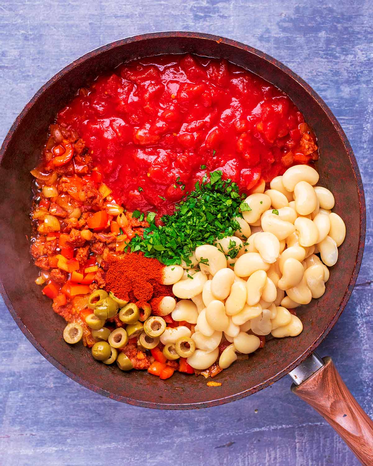 Tomatoes, butter beans, olives, chorizo, peppers, herbs and spices all cooking in a frying pan.