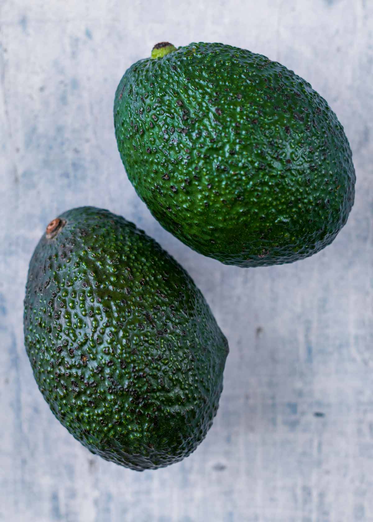 Two whole avocados on a wooden surface.