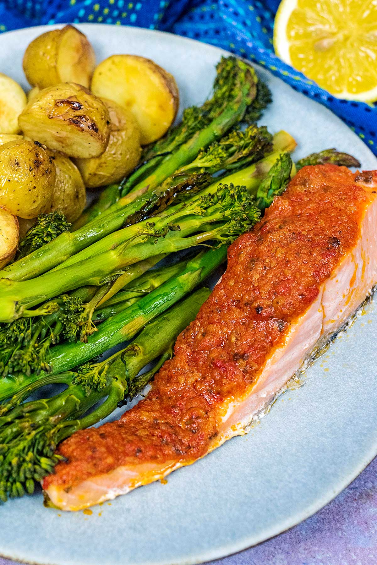Red pesto on top of cooked salmon next to vegetables and potatoes.