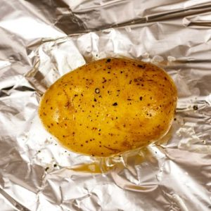 A seasoned whole potato on a sheet of foil.
