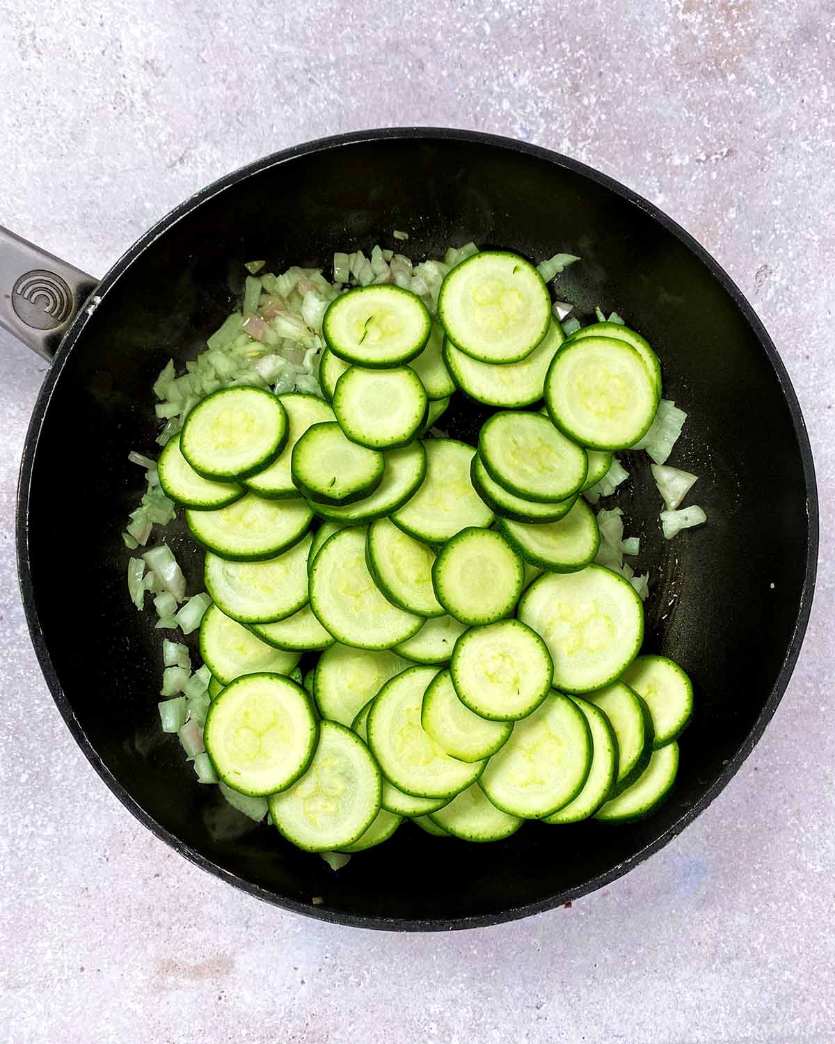 Chopped shallots and sliced courgettes in a frying pan.