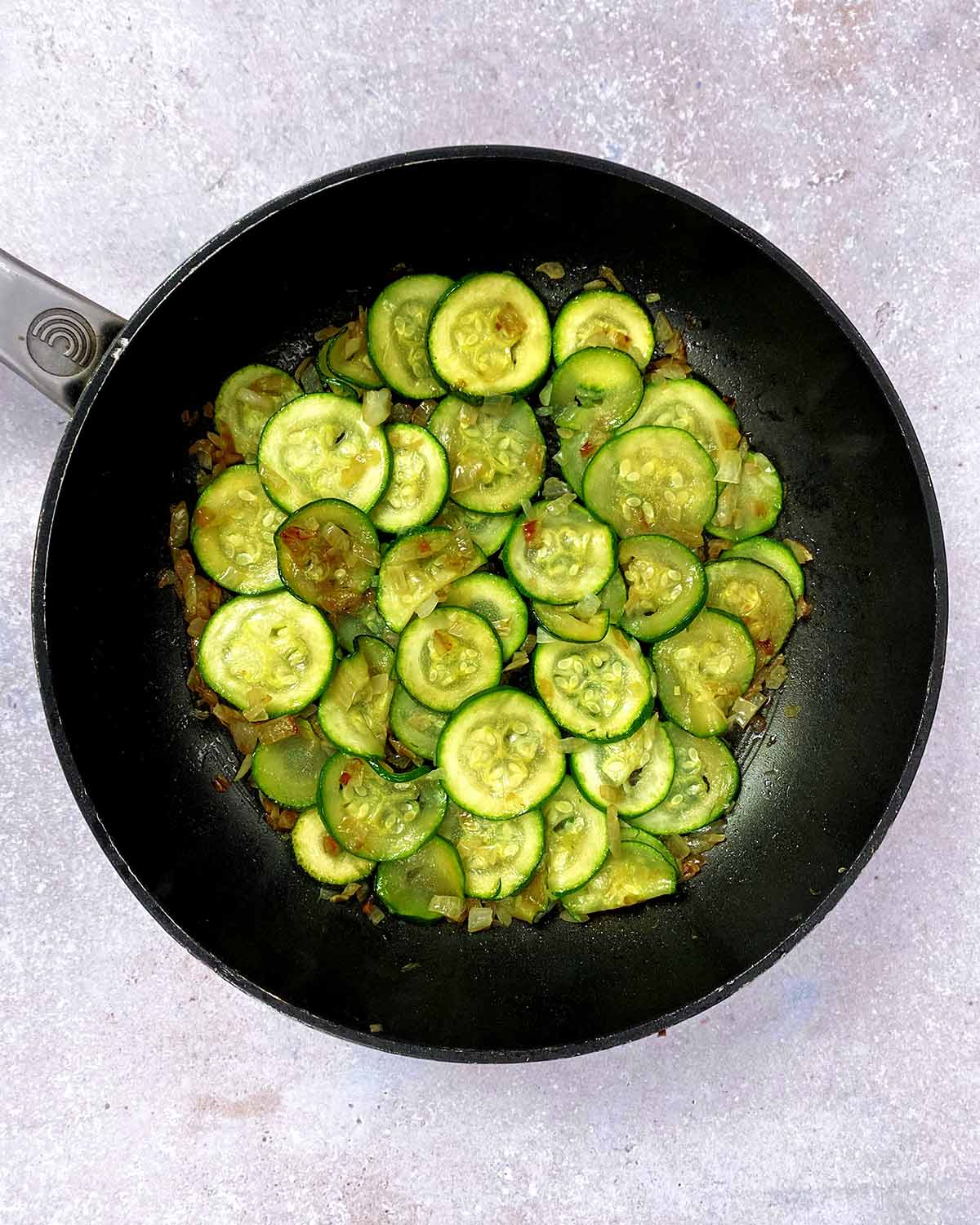Cooked chopped shallots and courgette slices in the pan.