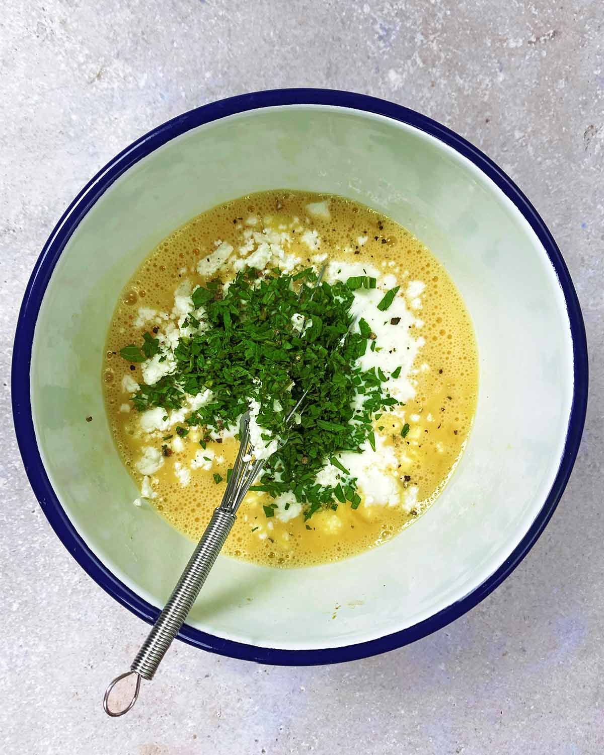 Whisked eggs, chopped mint leaves and seasoning in a bowl.