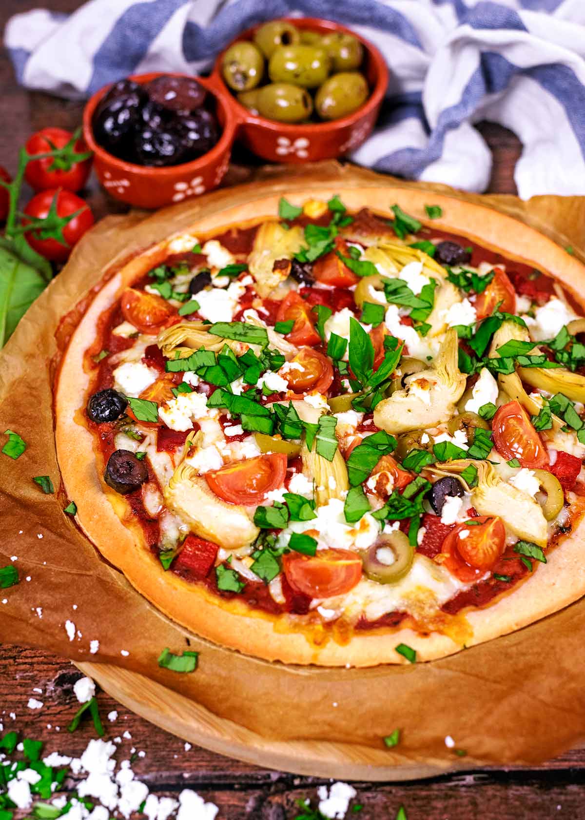 Pizza topped with chopped basil in front of a striped towel and a bowl of olives.
