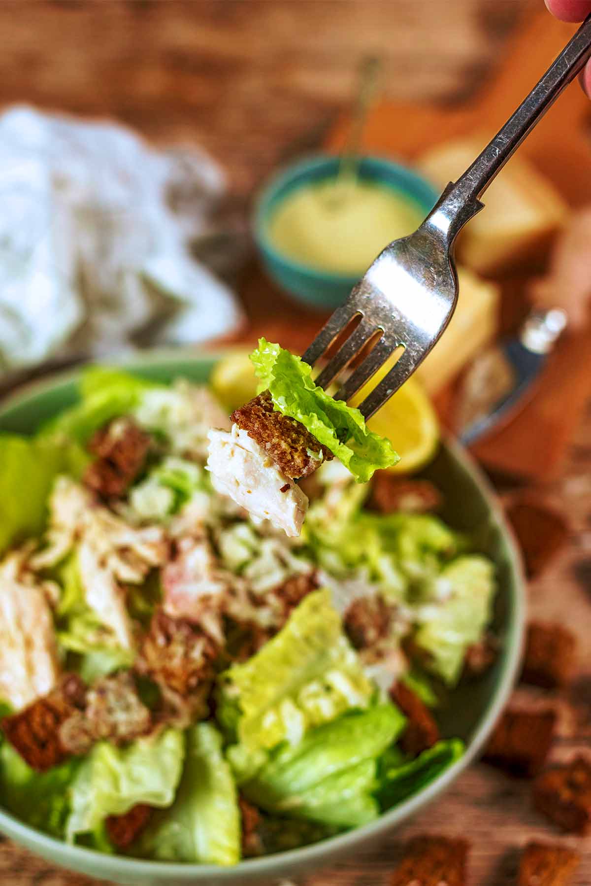 A fork picking up some lettuce, chicken and a crouton from a bowl of salad.