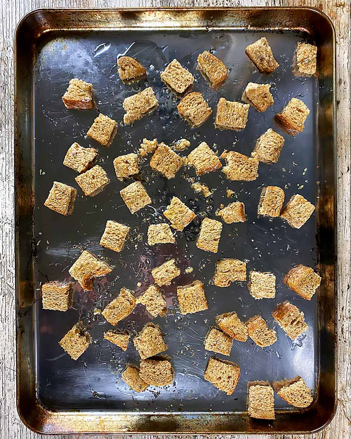 Cubes of bread spread out on a baking sheet covered in oil.