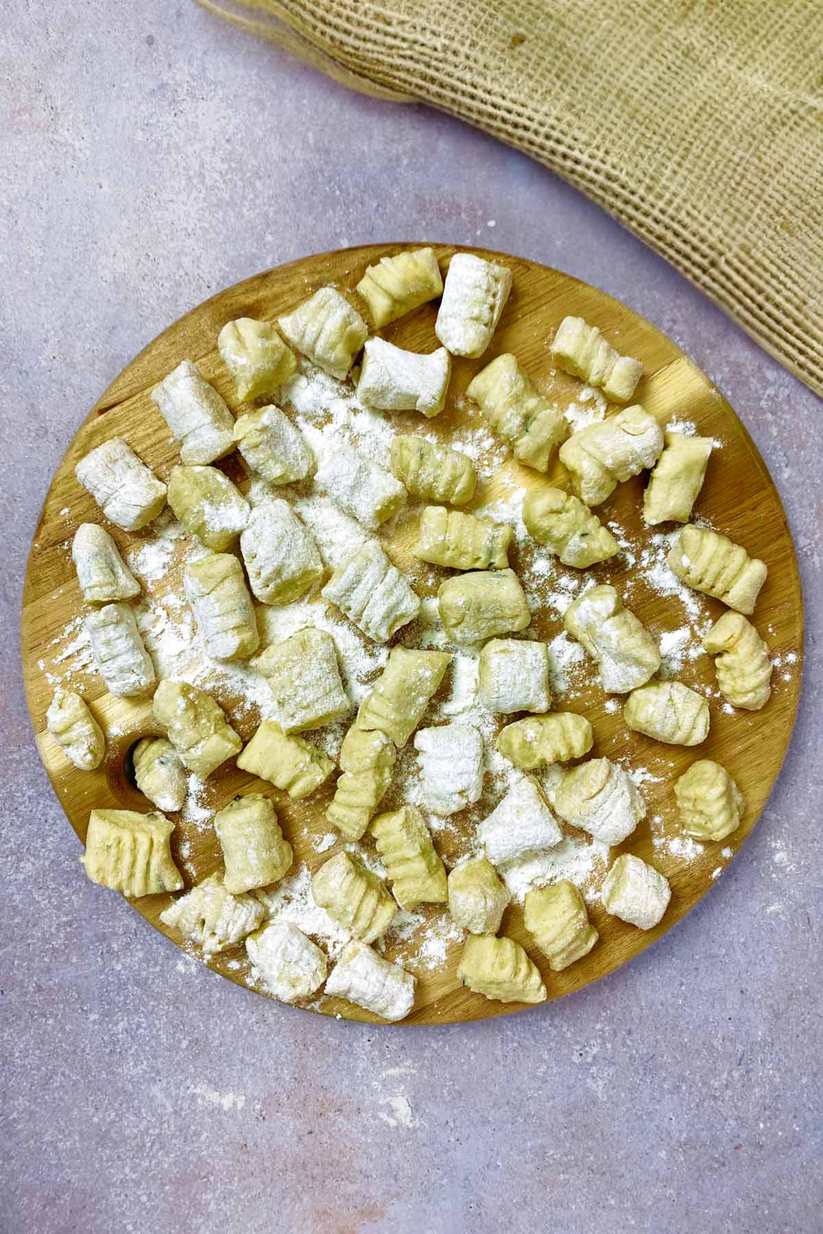 A round wooden serving board covered in uncooked gnocchi.