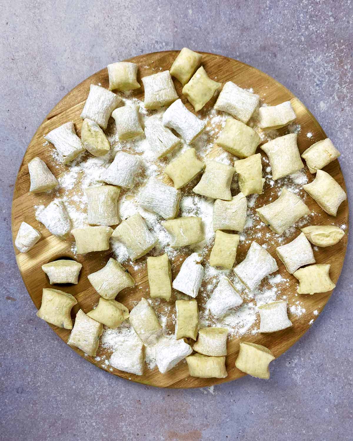 A wooden serving board covered in uncooked gnocchi.