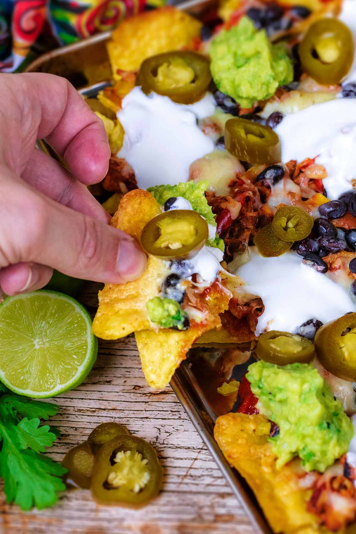 A hand holding a big scoop of nachos.