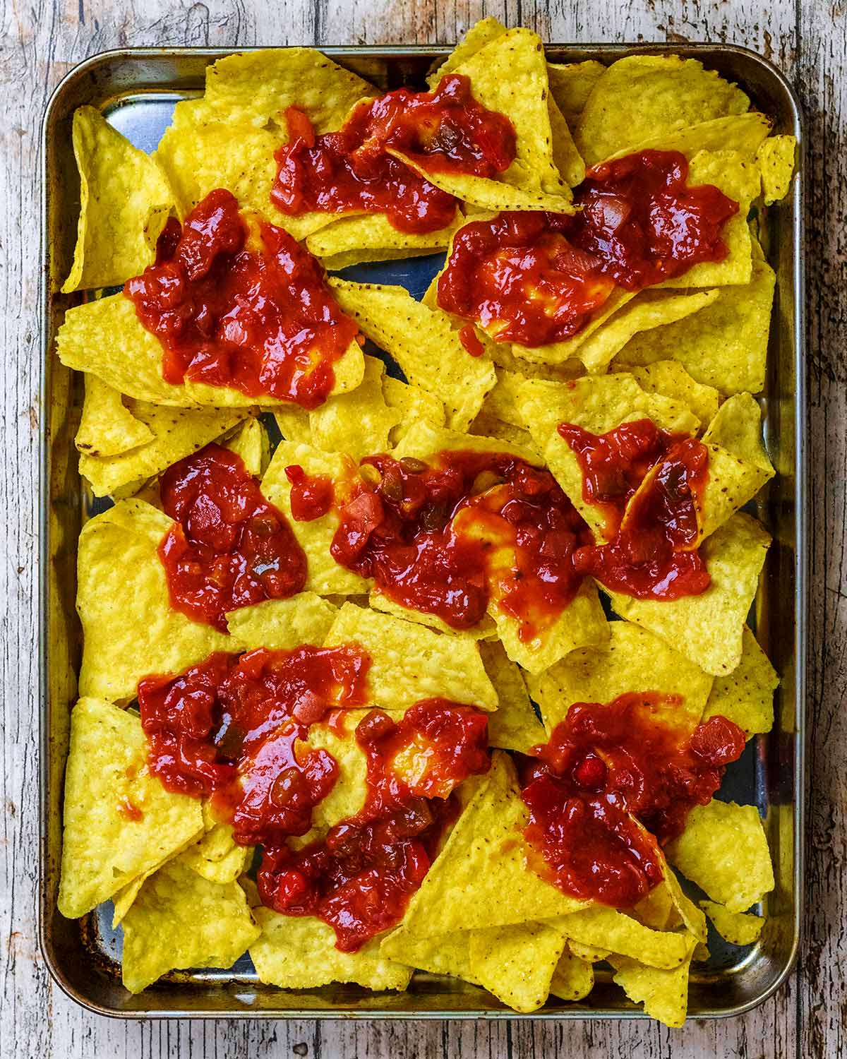 A baking tray covered in tortilla chips and dollops of salsa.