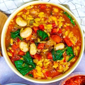 A bowl of orzo soup next to a checkered towel.