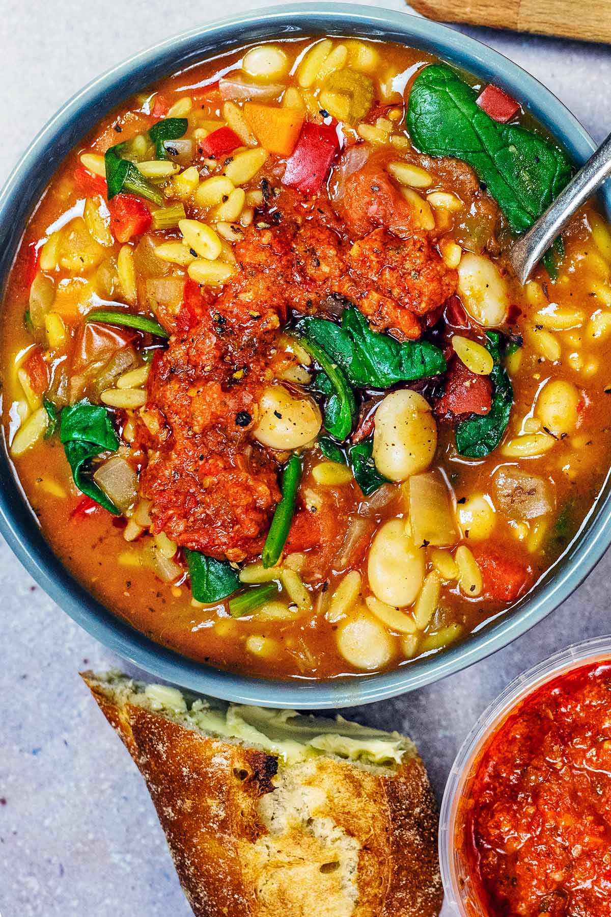 A bowl of orzo soup next to a pot of red pesto and some crusty bread.