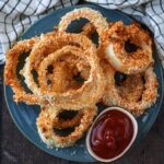 A plate of oven baked onion rings with a small pot of ketchup.