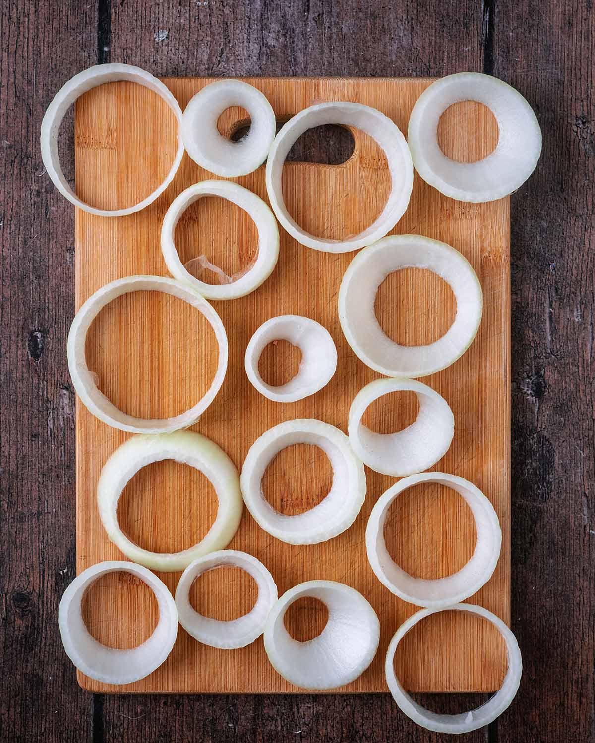 An onion cut into rings on a wooden chopping board.