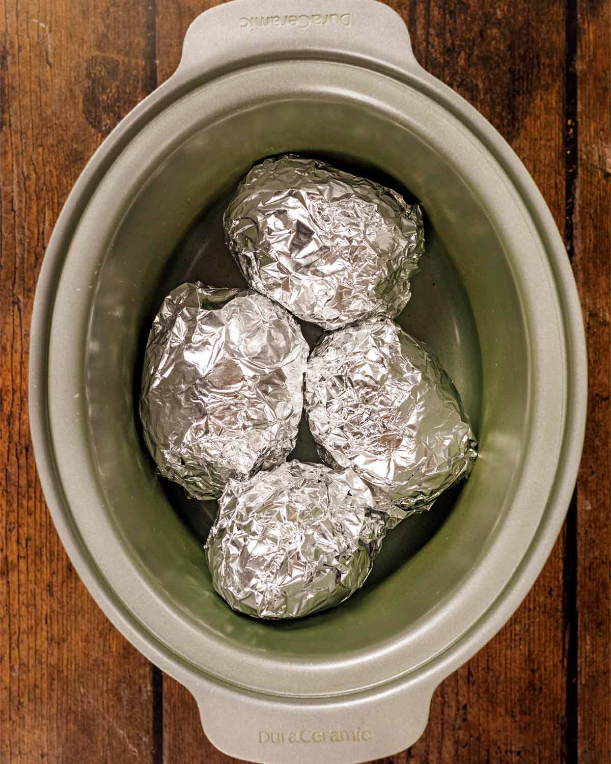 Four foil wrapped potatoes in a slow cooker.