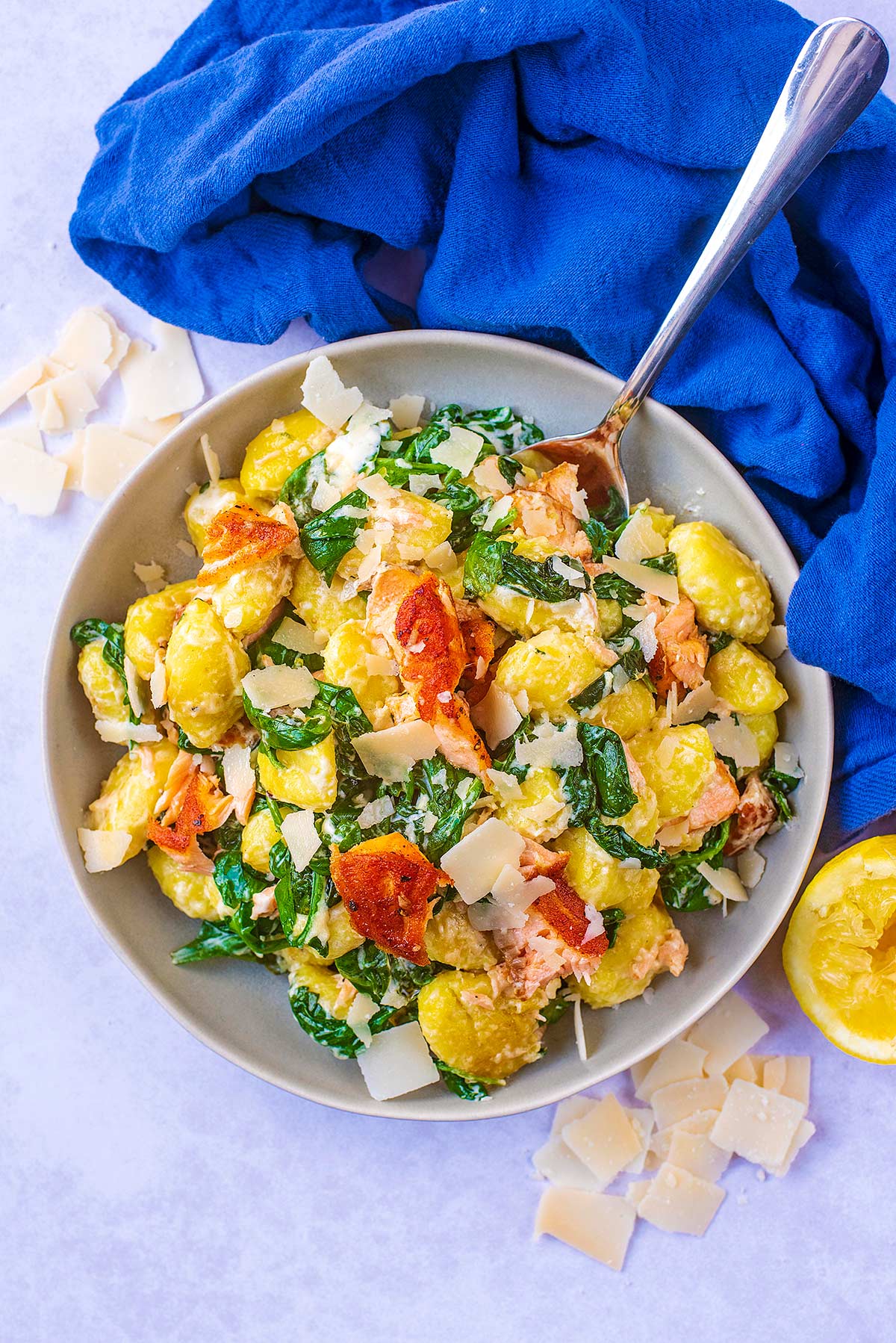 A bowl of gnocchi mixed with salmon and spinach next to a blue towel.