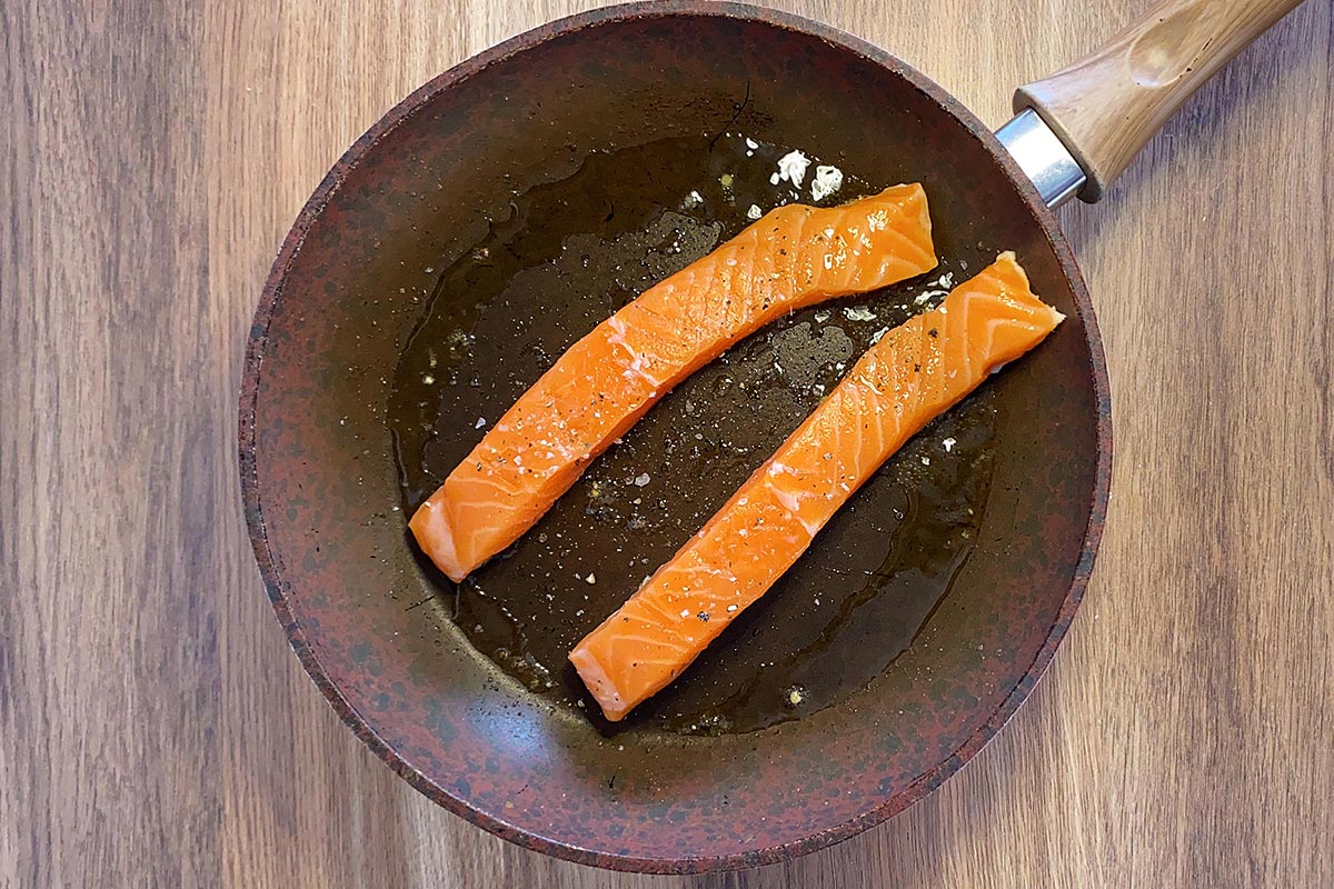 Two salmon fillets cooking in a frying pan.