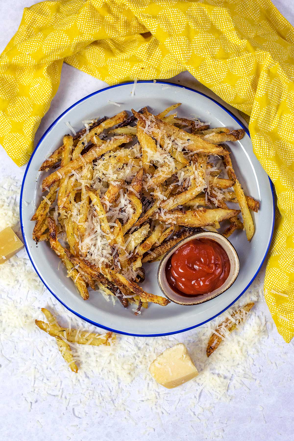 A plate of cheese covered fries with a small pot of ketchup.